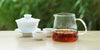 From left to right, a gaiwan, two teacups, and a glass server. The teacups and server have black tea in them.