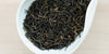 A white dish containing dry black tea leaves.