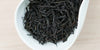 A white dish containing dry black tea leaves.