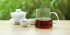 From left to right, a gaiwan, two teacups, and a glass server. The teacups and server have black tea in them.