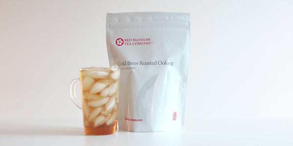 A glass cup filled with ice and Wuyi oolong tea next to a package of Cold Brew Roasted Oolon.