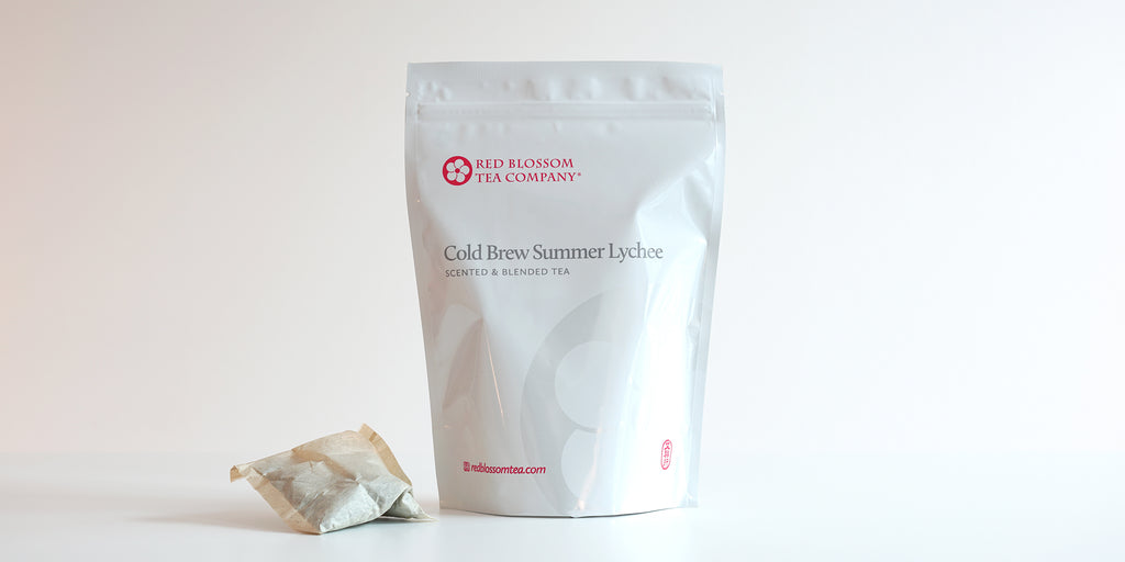A large teabag filled with lychee-scented black tea next to a package of Cold Brew Summer Lychee