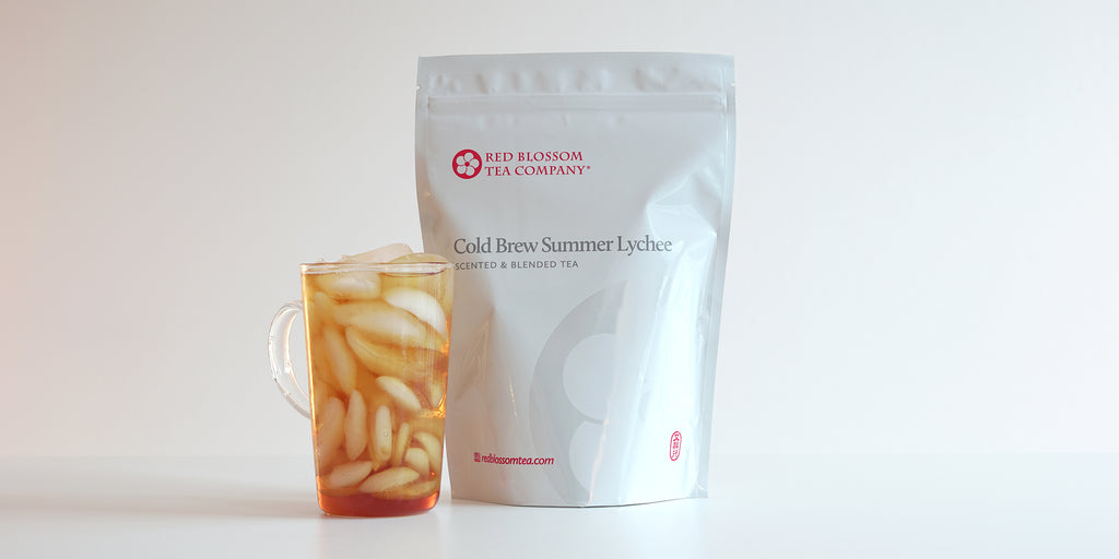 A glass cup filled with ice and lychee-scented black tea next to a package of Cold Brew Summer Lychee.