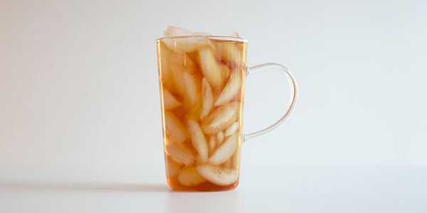 A glass cup filled with ice and lychee-scented black tea on a white background.