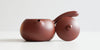Front view of a terracotta-colored yixing teapot. The lid is facing the camera, resting against the handle.