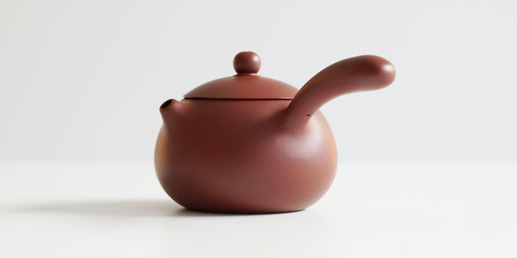 Front view of a terracotta-colored yixing pot highlighting the short spout and side handle.
