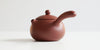 Front view of a terracotta-colored yixing pot highlighting the short spout and side handle.