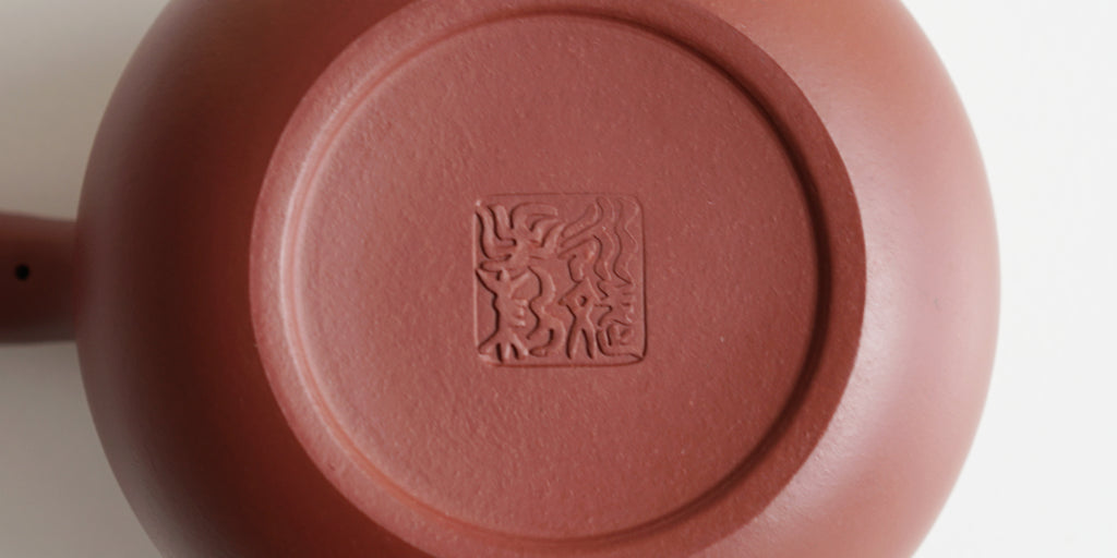The bottom of a terracotta-colored yixing teapot. A maker’s mark is stamped into the base.