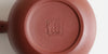 The bottom of a terracotta-colored yixing teapot. A maker’s mark is stamped into the base.