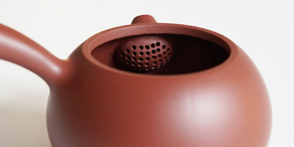 Rear view of the inside of a terracotta-colored yixing pot, showcasing the built-in filter made by punching small holes in the clay.