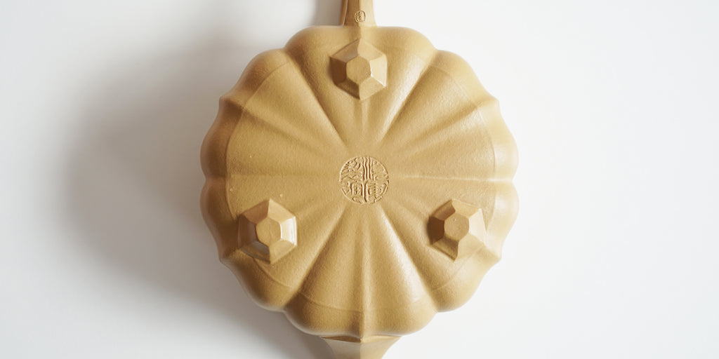 The bottom of a yellow yixing teapot. A maker’s mark is stamped into the base, and three hexagonal feet are around the outside.