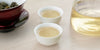 Two small teacups of jasmine tea, with a gaiwan in the background on the left and a glass server on the right.