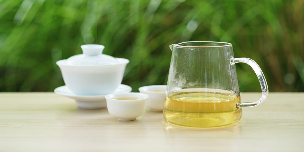From left to right, a gaiwan, two teacups, and a glass server. The teacups and server have Formosa oolong tea in them.