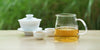 From left to right, a gaiwan, two teacups, and a glass server. The teacups and server have Formosa oolong tea in them.