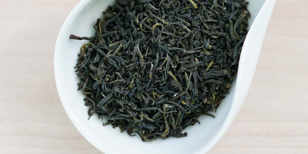 A white dish containing dry green tea leaves.