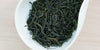 A white dish containing dry green tea leaves.