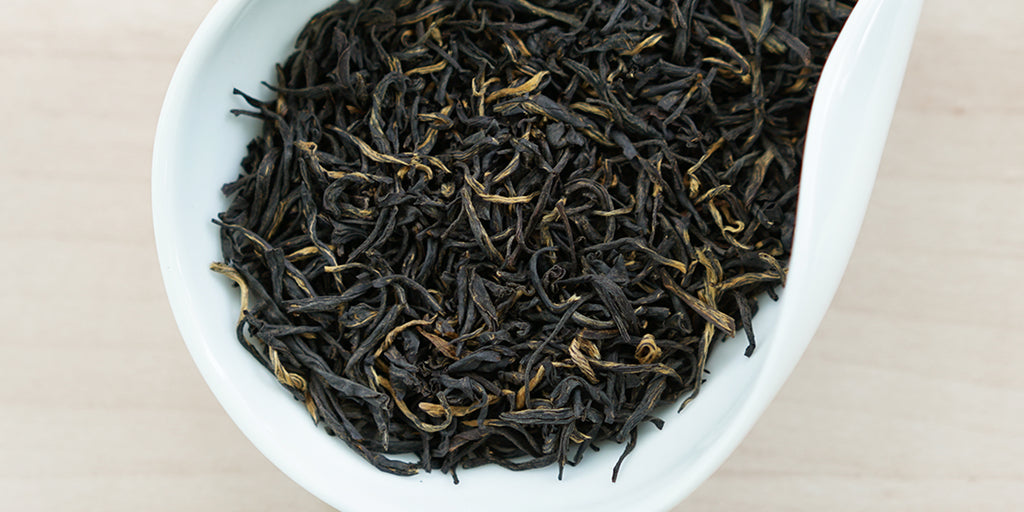 A white dish containing dry black tea leaves.