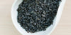 A white dish containing dry green tea leaves.