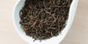 A white dish containing dry pu-erh tea leaves.