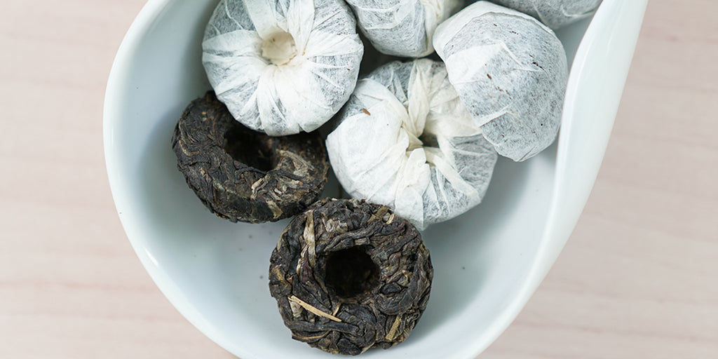 A white dish containing tuos of pu-erh tea wrapped in white paper.