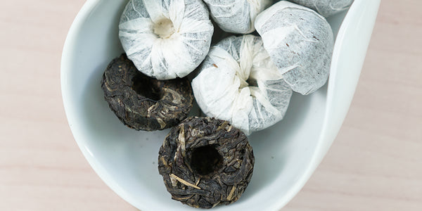 A white dish containing tuos of pu-erh tea wrapped in white paper.