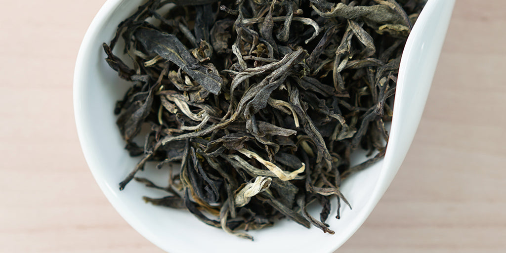 A white dish containing dry pu-erh tea leaves.