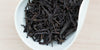 A white dish containing dry Phoenix oolong tea leaves.