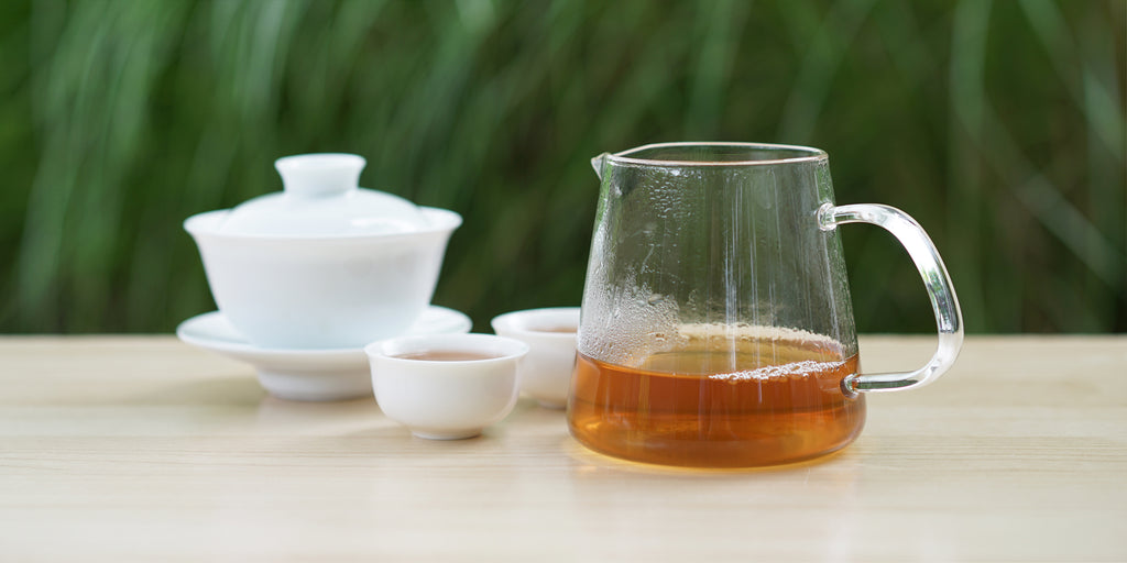 From left to right, a gaiwan, two teacups, and a glass server. The teacups and server have Phoenix oolong tea in them.