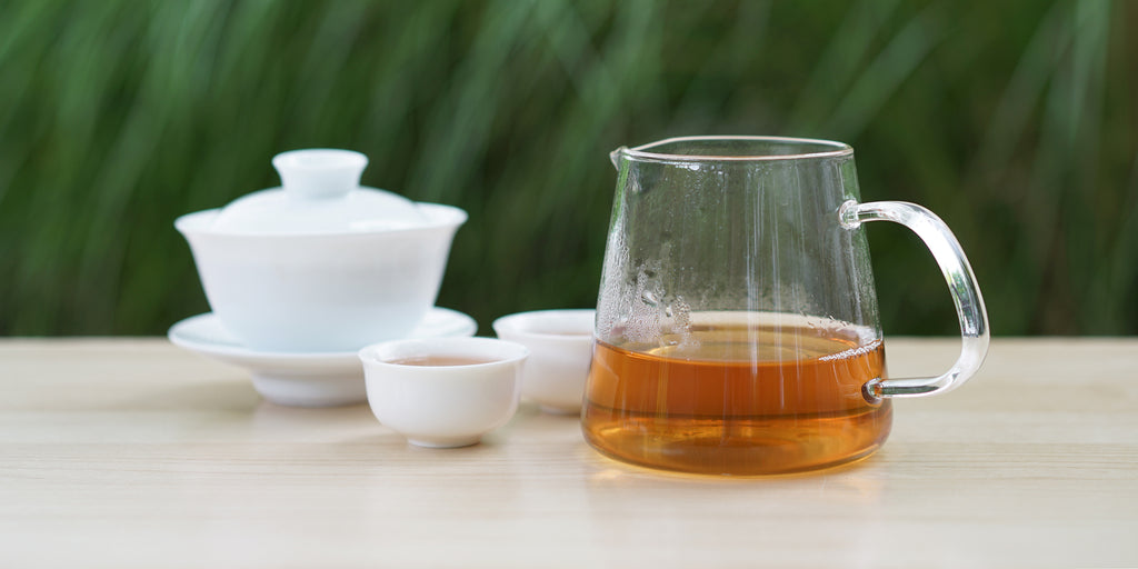 From left to right, a gaiwan, two teacups, and a glass server. The teacups and server have Phoenix oolong tea in them.