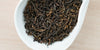 A white dish containing dry pu-erh tea leaves.
