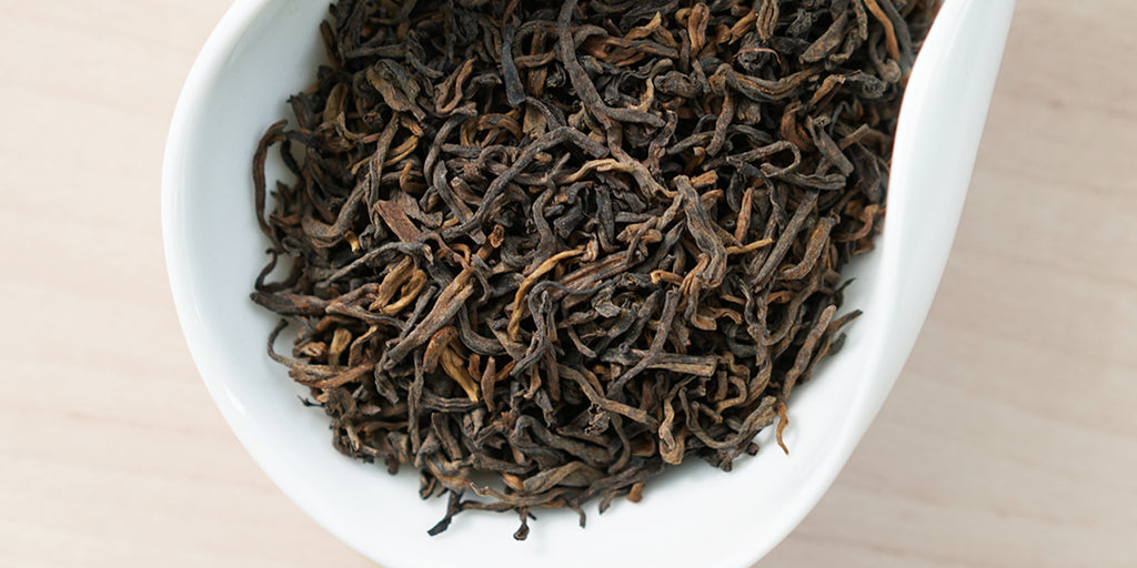 A white dish containing dry pu-erh tea leaves.