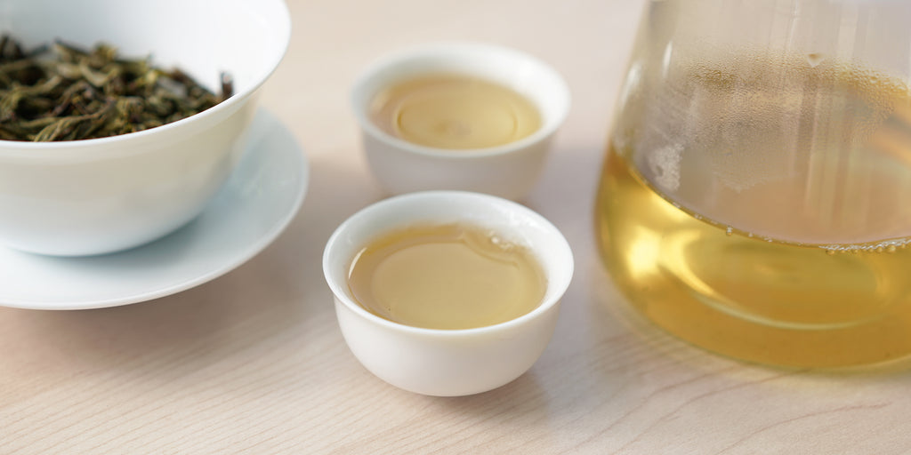 Two small teacups of pu-erh tea, with a gaiwan in the background on the left and a glass server on the right.