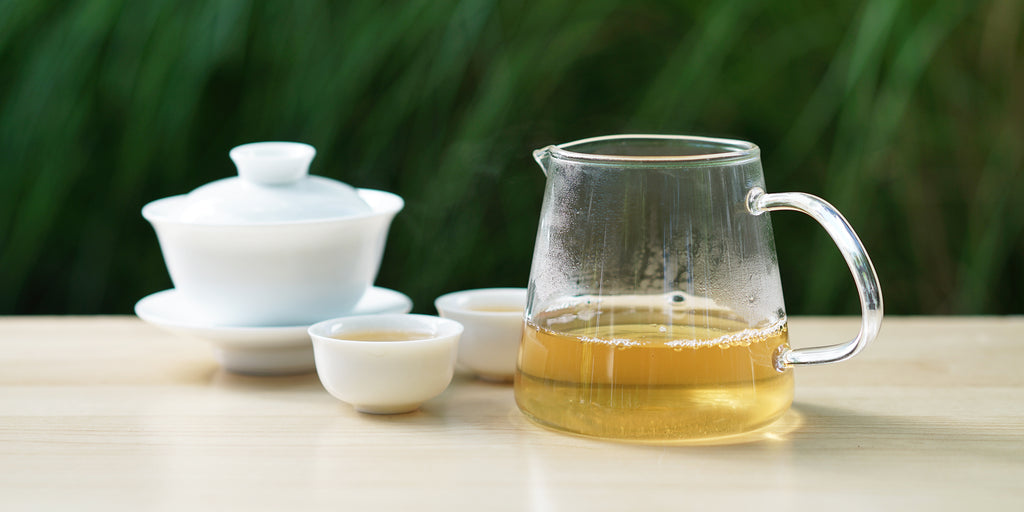 From left to right, a gaiwan, two teacups, and a glass server. The teacups and server have pu-erh tea in them.