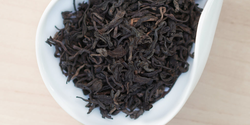 A white dish containing dry pu-erh tea leaves.
