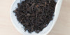 A white dish containing dry pu-erh tea leaves.