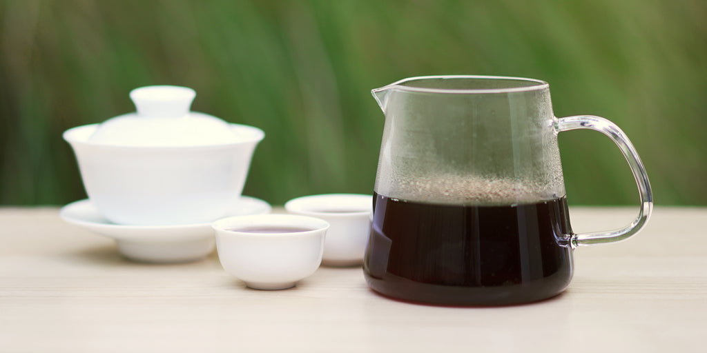 From left to right, a gaiwan, two teacups, and a glass server. The teacups and server have pu-erh tea in them.