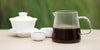 From left to right, a gaiwan, two teacups, and a glass server. The teacups and server have pu-erh tea in them.