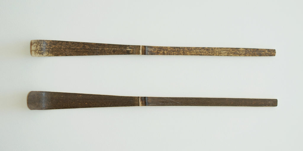 A pair of purple bamboo matcha scoops next to each other, slightly different in color due to the natural variation.