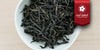 A white dish containing dry Phoenix oolong tea leaves. A red ribbon in the top right corner reads “Red Label Collection”