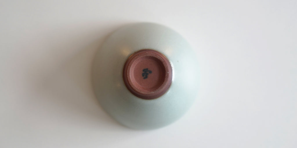 The bottom of a blue-green celadon teacup. Xu De Jia's maker's mark is painted on the unglazed foot in black.