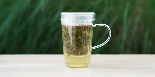 A glass cup with genmaicha brewing in the nested glass infuser.