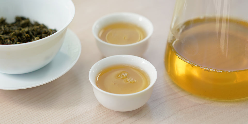 Two small teacups of jasmine tea, with a gaiwan in the background on the left and a glass server on the right.