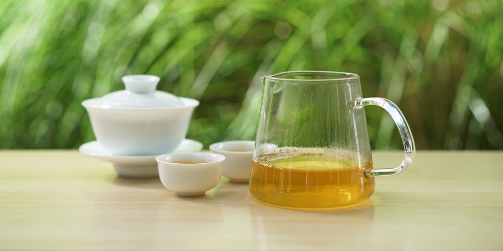 From left to right, a gaiwan, two teacups, and a glass server. The teacups and server have jasmine tea in them.