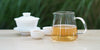 From left to right, a gaiwan, two teacups, and a glass server. The teacups and server have jasmine tea in them.