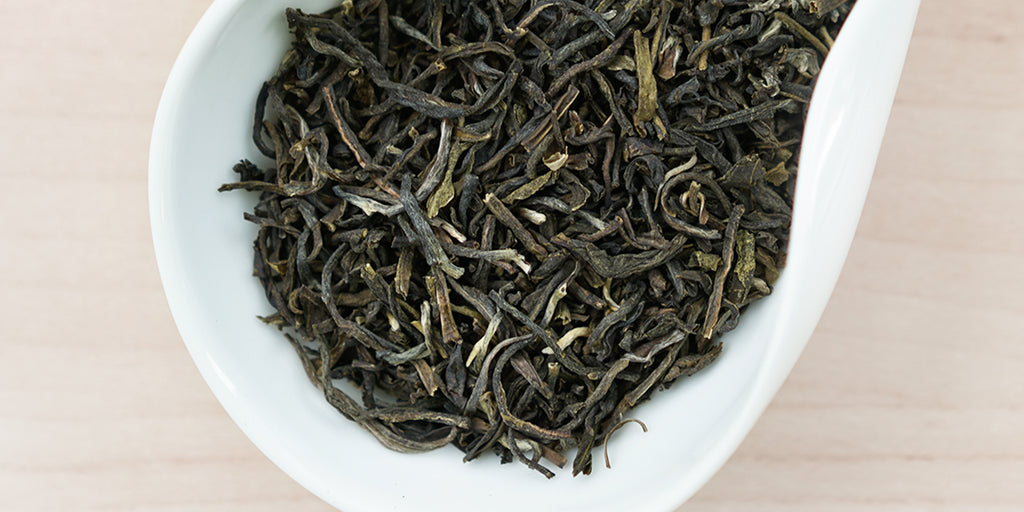 A white dish containing dry jasmine tea leaves.