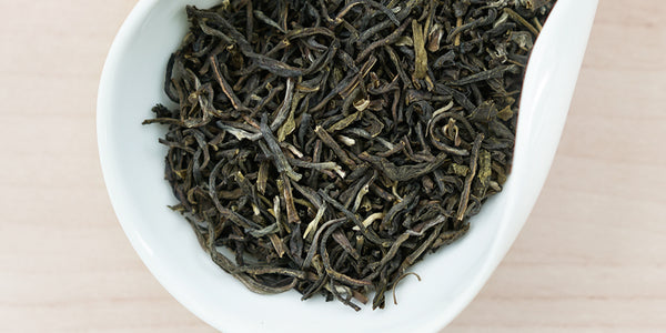 A white dish containing dry jasmine tea leaves.