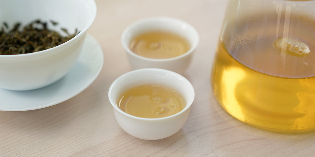 Two small teacups of jasmine tea, with a gaiwan in the background on the left and a glass server on the right.