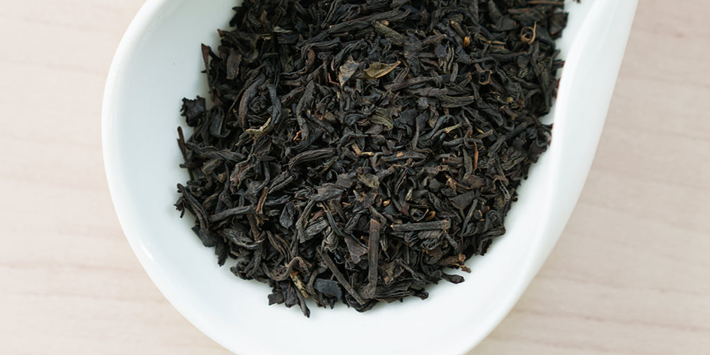 A white dish containing dry black tea leaves.