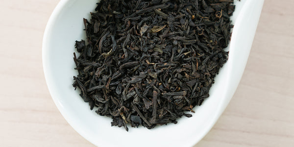 A white dish containing dry black tea leaves.