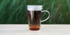 A glass cup with lychee black brewing in the nested glass infuser.